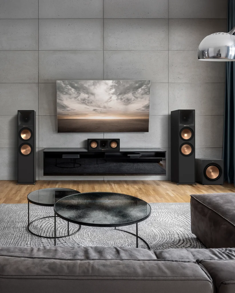 A home cinema against a concrete wall: floorstanding speakers either side of a wall-mounted television, with a centre speaker and subwoofer.