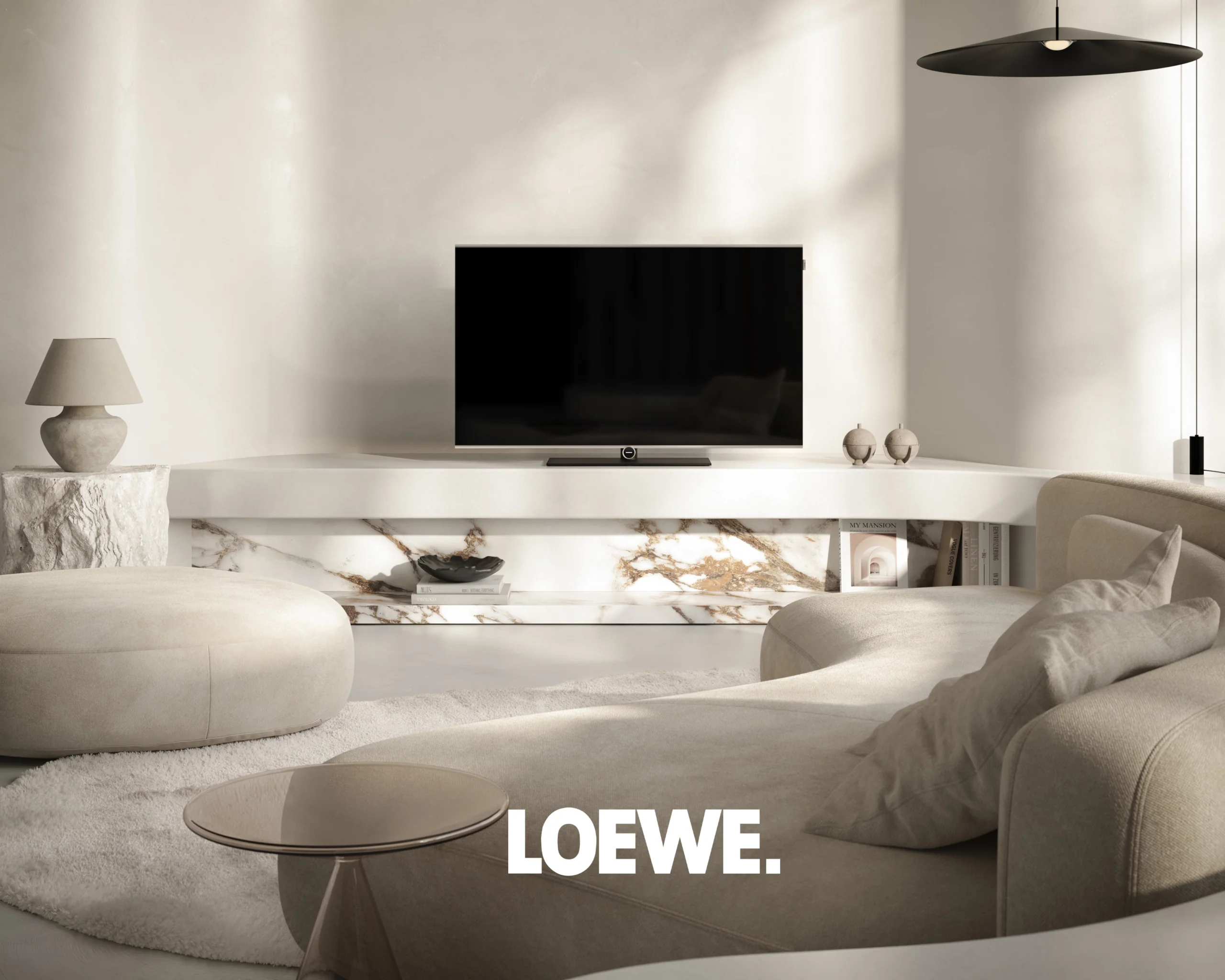 A Loewe television on a pale stone ledge in a cream living room, with a curved sofa and a black pendant light.