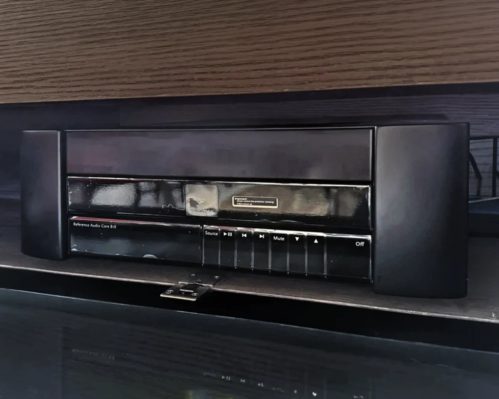 Black source component on a glossy shelf, with transport and volume controls along its front panel