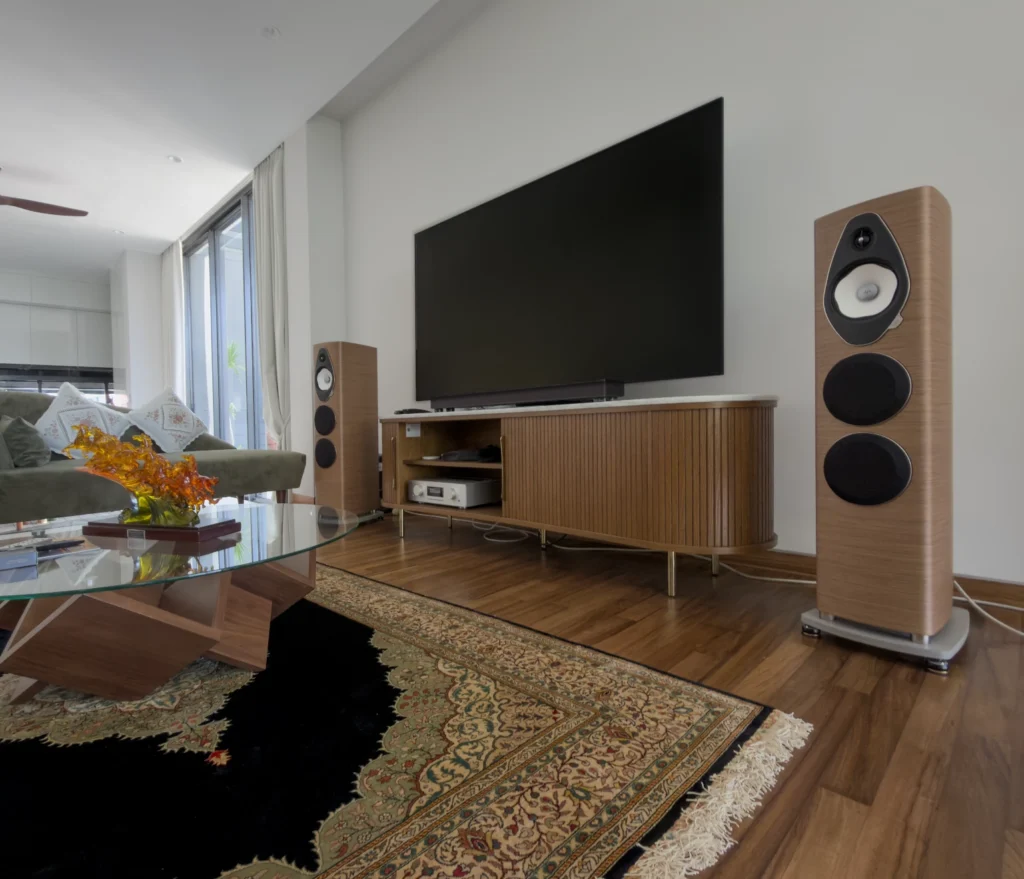 Walnut Sonus Faber floorstanding loudspeakers either side of a television on a fluted timber sideboard, with an AVM amplifier on the shelf below.