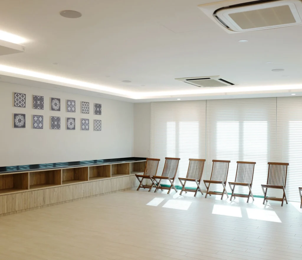 Recessed ceiling loudspeakers in a condominium function room, above timber cabinetry and folding chairs set along shuttered windows.