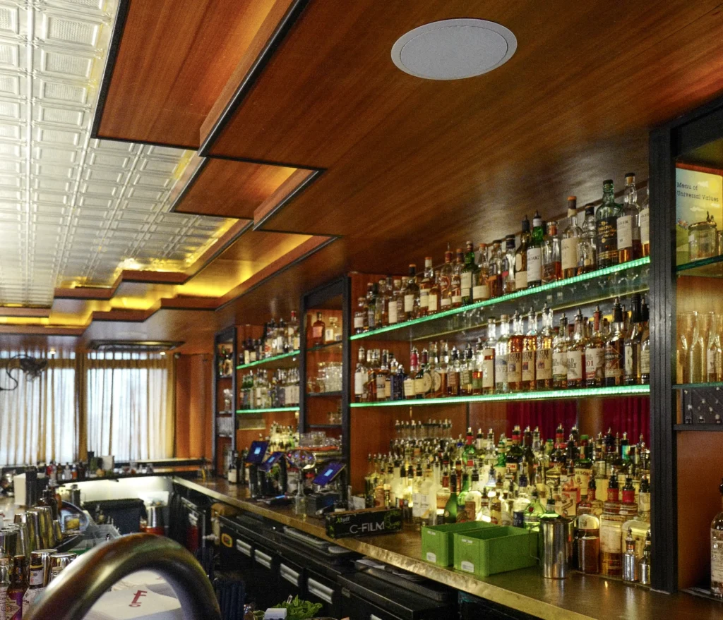 A bar at Regency Park condominium, with a recessed ceiling loudspeaker above backlit shelves of bottles.