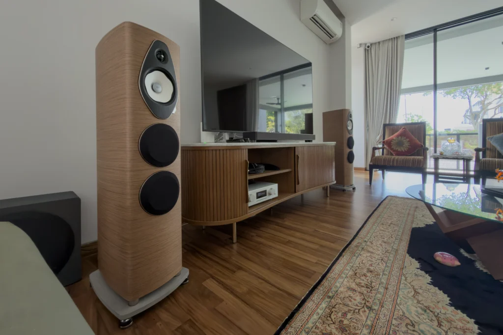 A pair of walnut Sonus Faber floorstanding loudspeakers either side of a fluted wooden sideboard holding an AVM amplifier, below a wall-mounted television.