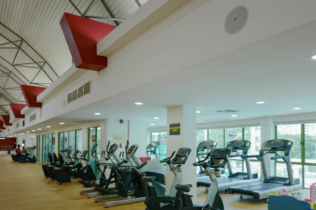 Gym floor with rows of cardio machines and a round ceiling speaker overhead