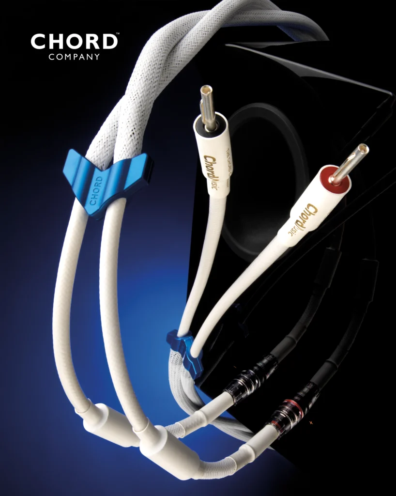 Chord Company white speaker cable with banana plugs and a blue cable clip, against a dark speaker.