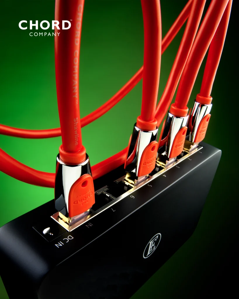 Red Chord Company network cables with polished metal plugs connected to a black network switch, on a green background.