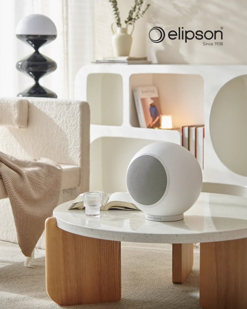 White Elipson spherical speaker on a stone-topped coffee table in a bright cream living room.