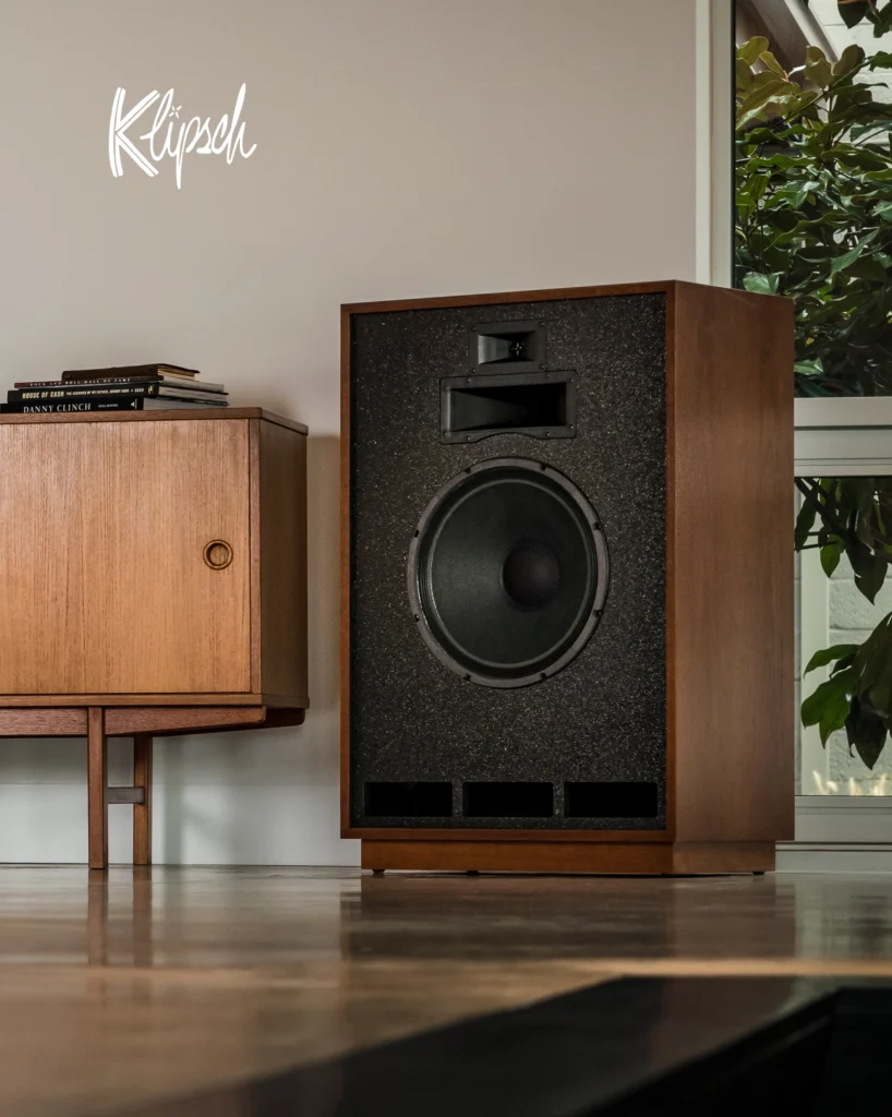 Klipsch horn-loaded floorstanding speaker in a walnut cabinet beside a mid-century sideboard in a bright room.