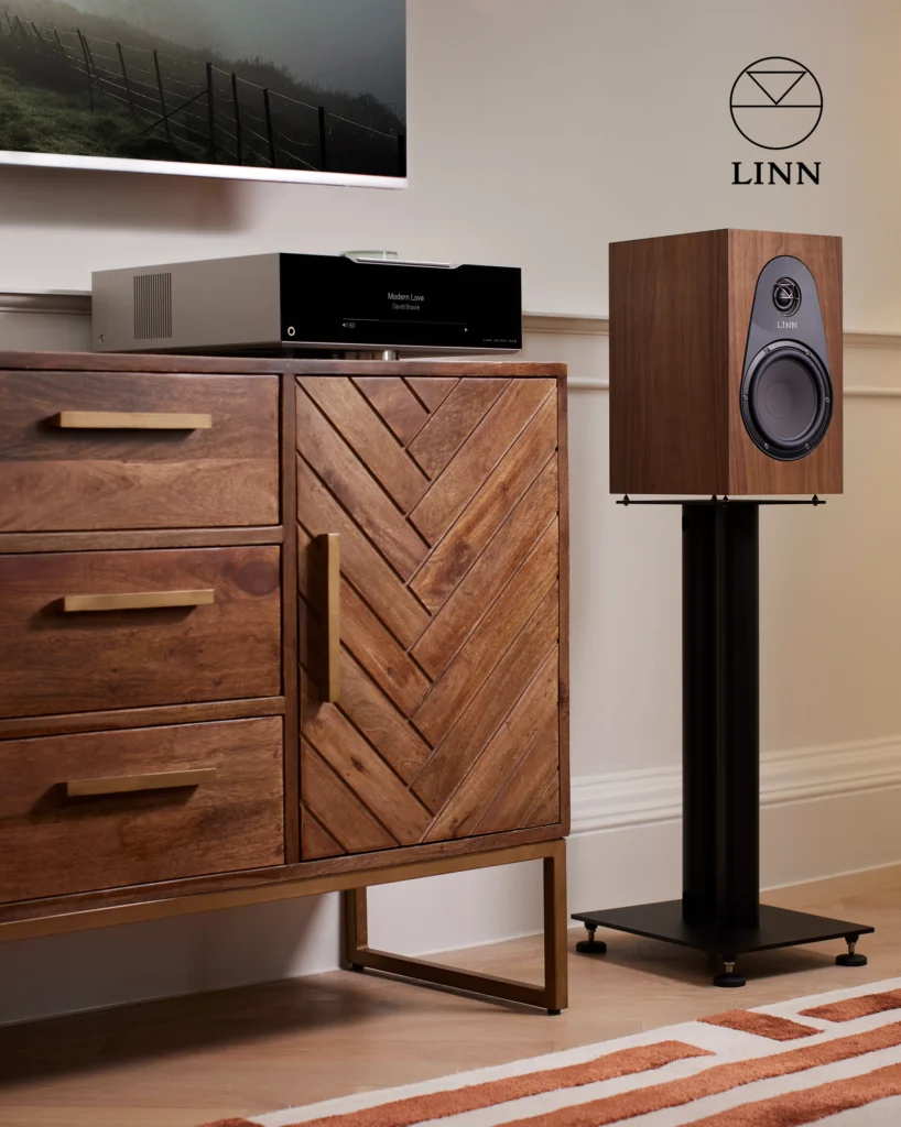 Linn network player and a walnut Linn bookshelf speaker on a stand beside a herringbone wooden sideboard.