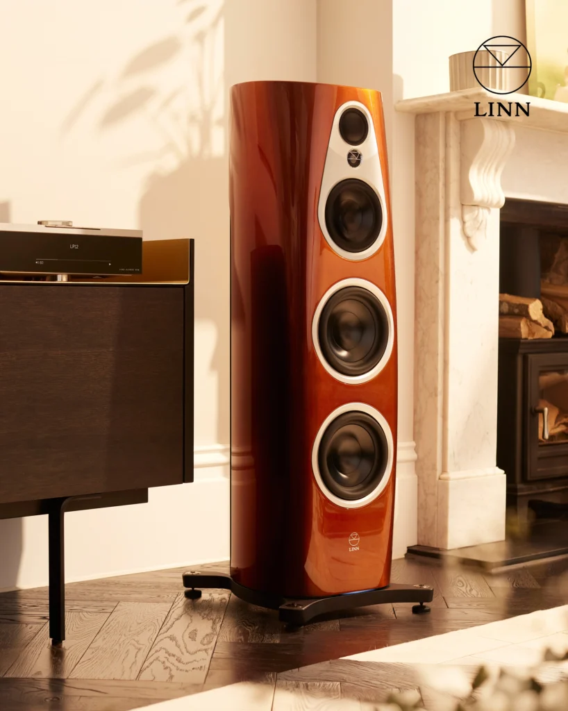 Tall Linn floorstanding speaker in a glossy copper-brown finish beside a dark cabinet and a fireplace.