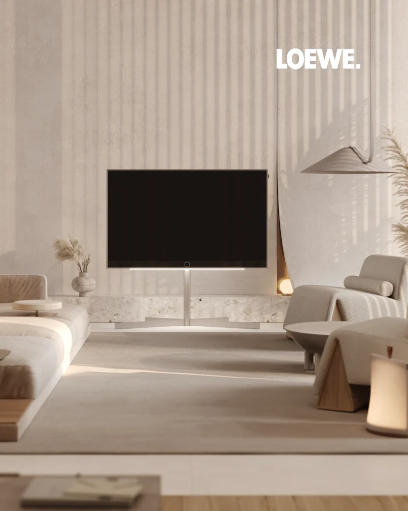 A freestanding Loewe television on a pedestal stand in a beige living room, beside a terrazzo-clad console.