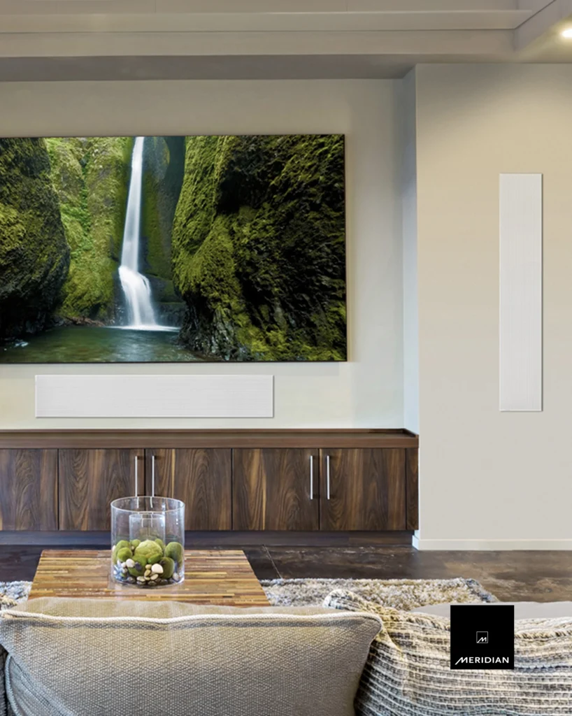 Slim white Meridian in-wall speakers beside a wall-mounted television above a walnut media cabinet.