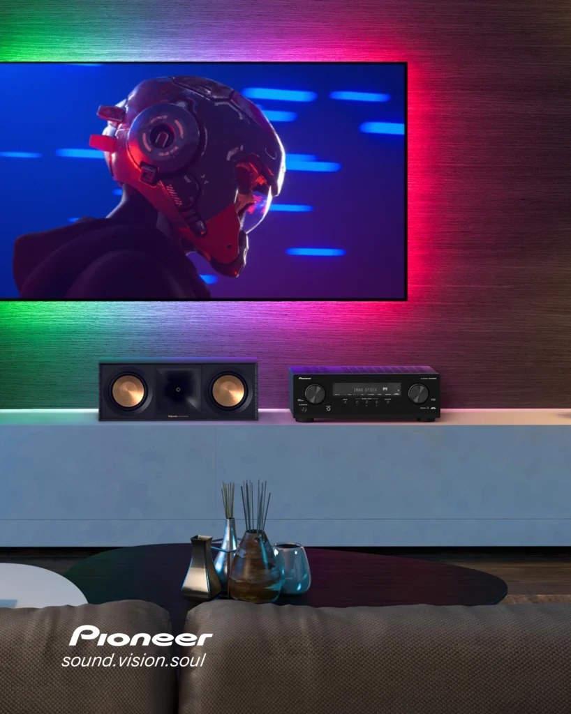 Pioneer AV receiver and a centre speaker on a low unit beneath a wall-mounted television with coloured backlighting.