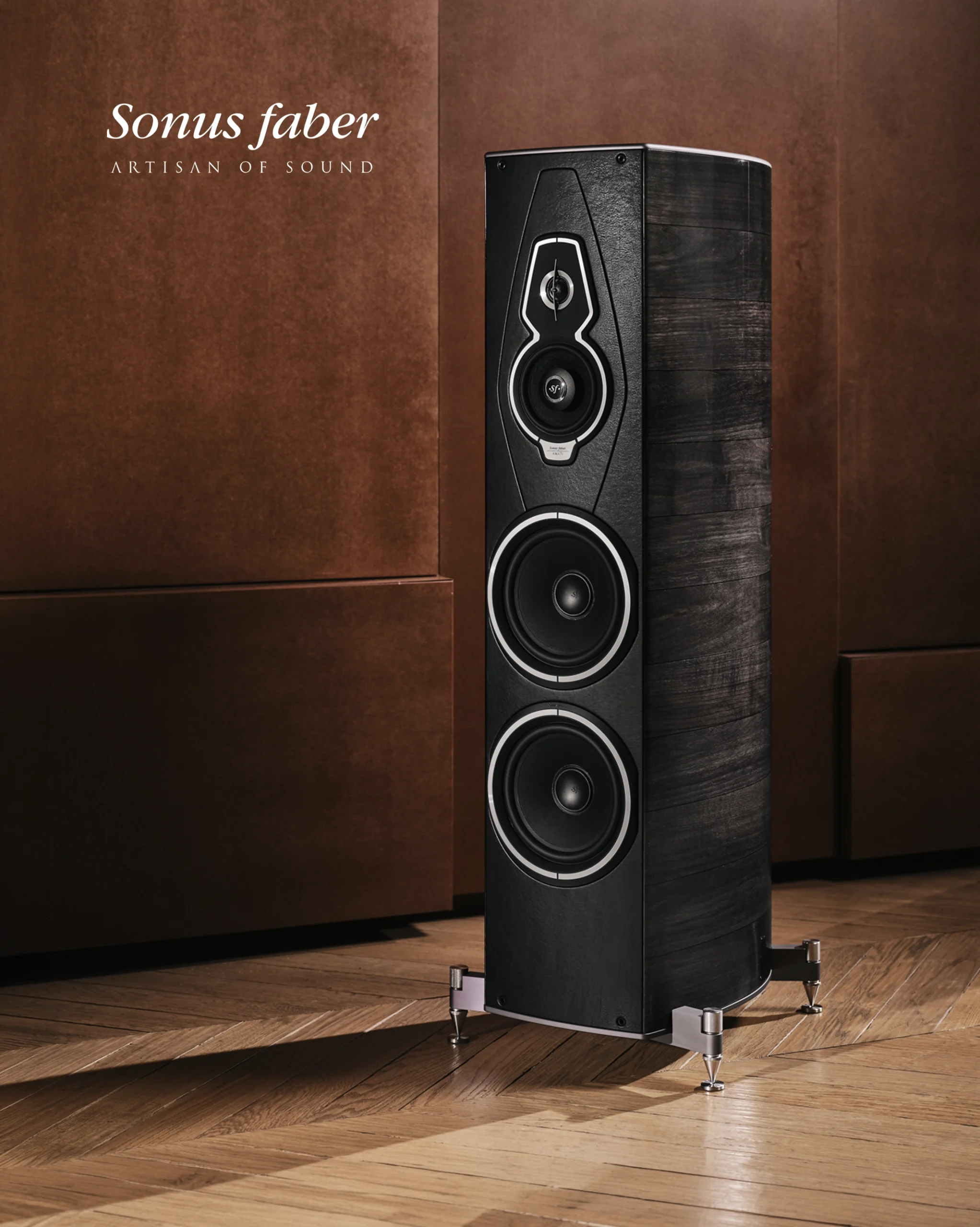 Black Sonus Faber floorstanding speaker with chrome feet in front of tan leather panelling.