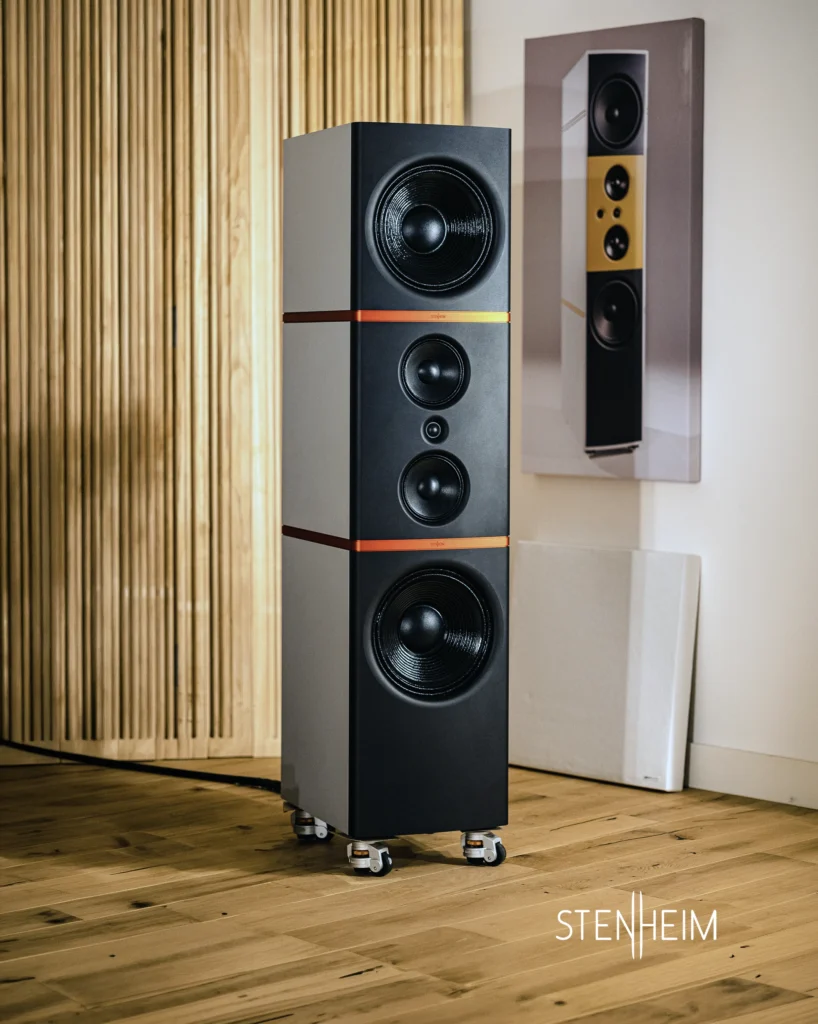 Stenheim floorstanding speaker on castors in a wood-floored room with slatted wall panels.