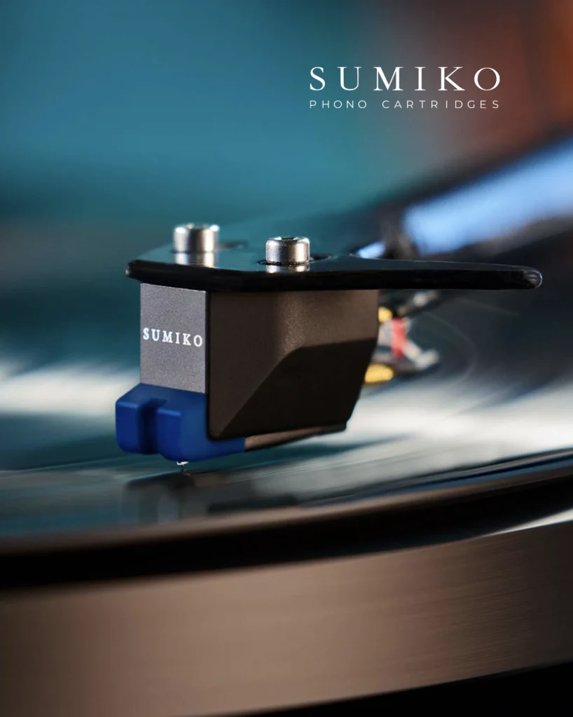 Sumiko phono cartridge with a blue stylus housing tracking a record against a teal background.