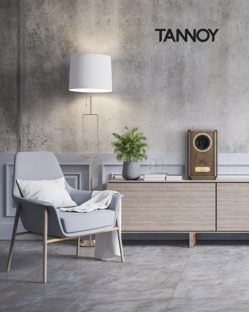 Small Tannoy speaker with a gold dual-concentric driver on a pale sideboard beside a grey armchair and floor lamp.