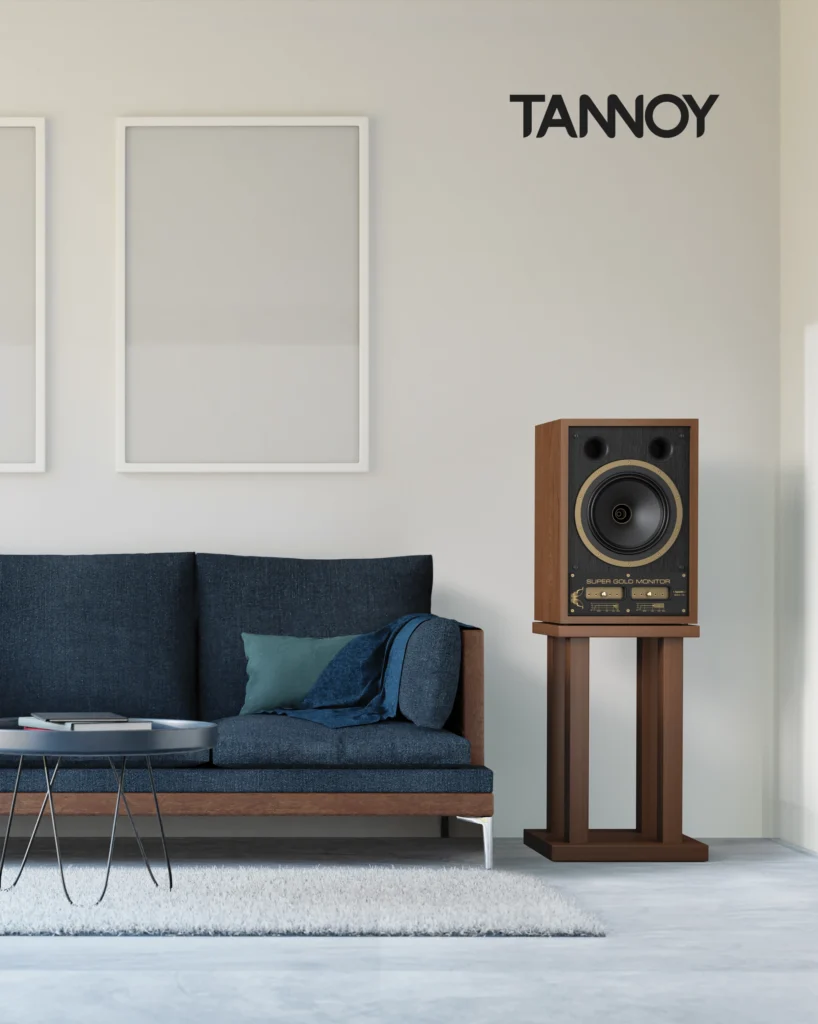 Tannoy bookshelf speaker on a wooden stand beside a navy sofa in a pale living room.
