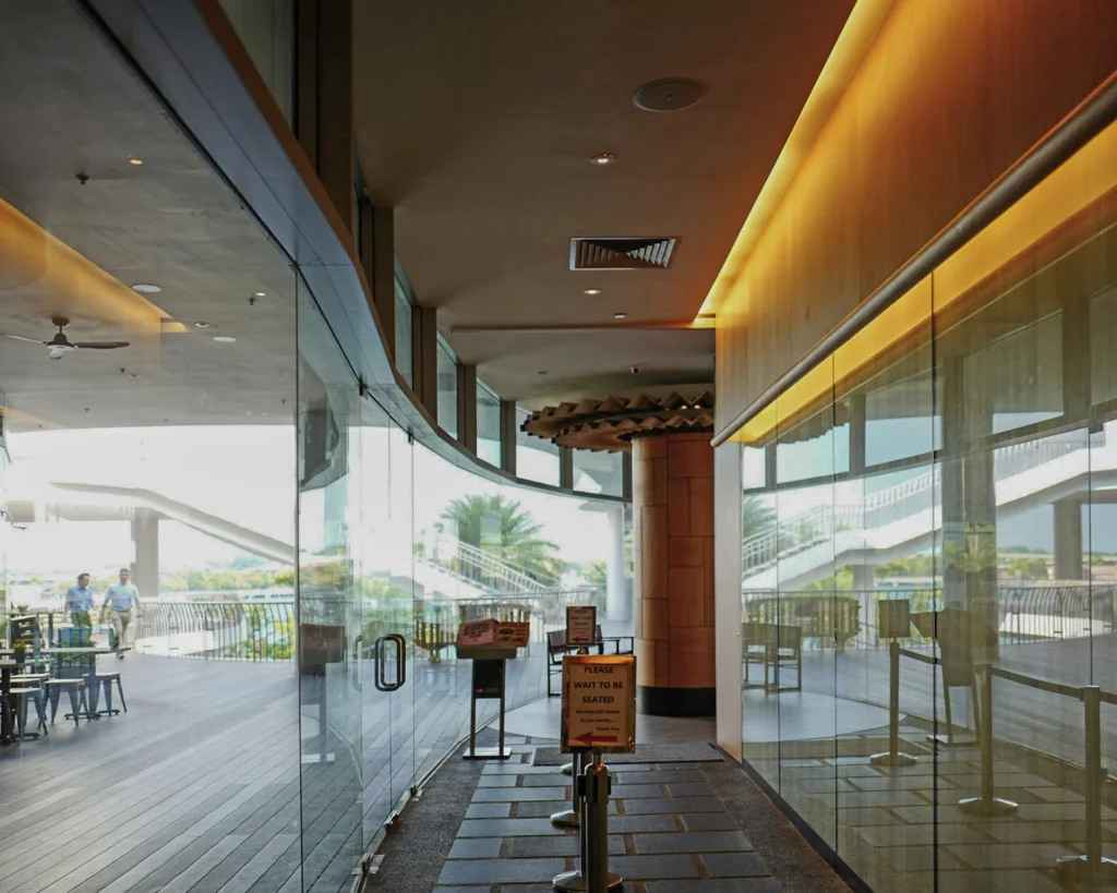 Glass-fronted entrance walkway at the restaurant with a ceiling speaker and warm cove lighting