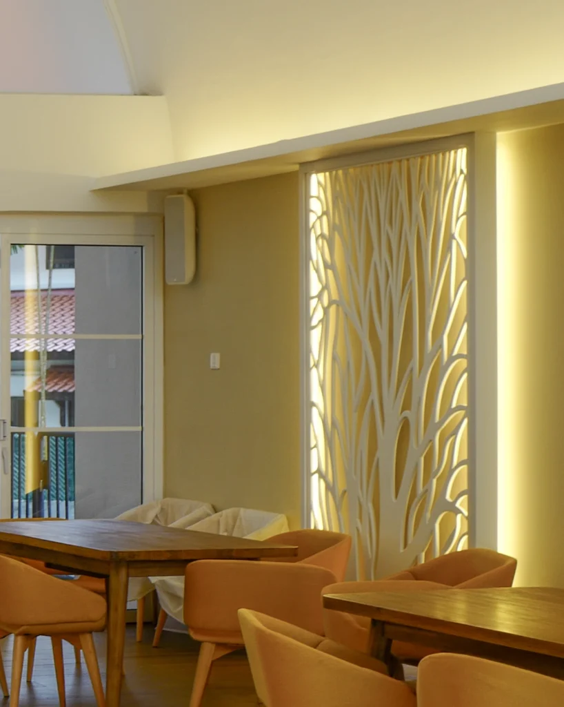 A warmly lit dining room with a carved white screen, orange armchairs and a small speaker on the wall
