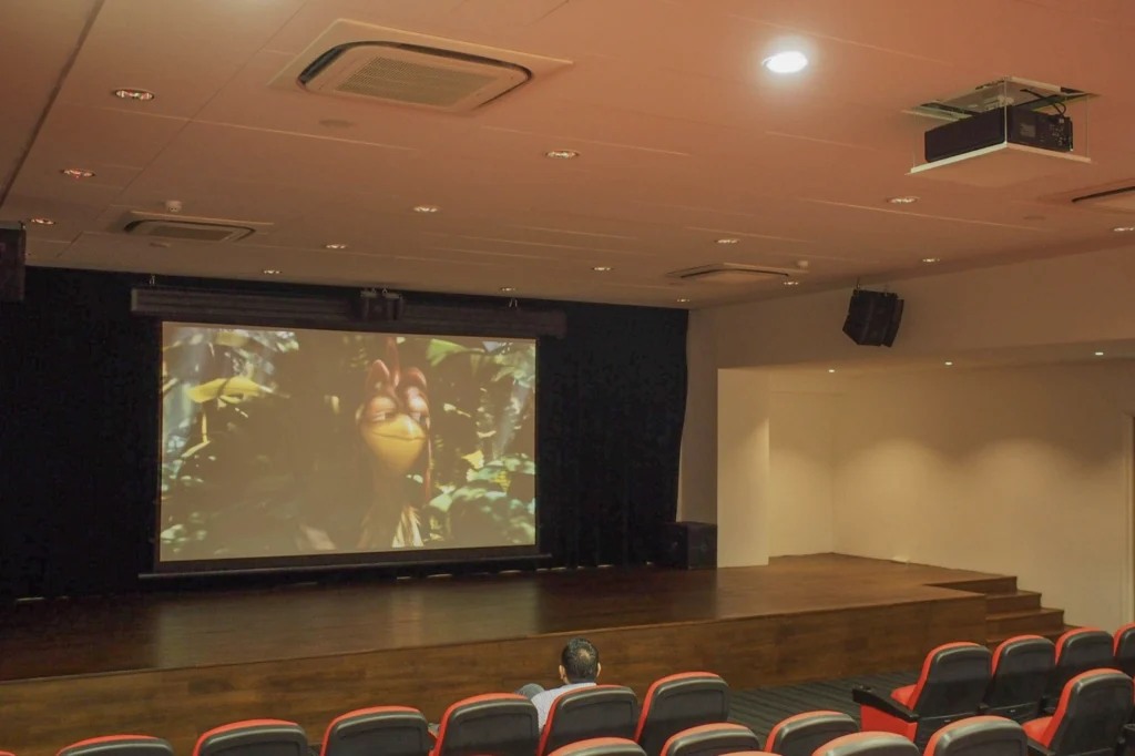 Projection screen and wall speaker at the front of a corporate function room and theatre, with red tiered seating