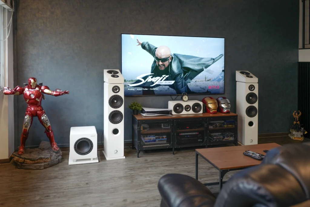 An Elipson Prestige Facet 5.1.2 home theatre system in white, with floorstanding speakers either side of a wall-mounted television and a subwoofer to the left.