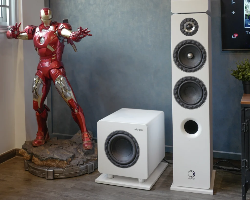A white Elipson Prestige Facet floorstanding speaker and matching subwoofer standing against the wall.