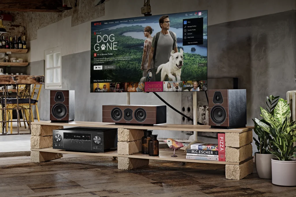 Two bookshelf speakers and a centre speaker in dark wood with an AV receiver on a low stand below a wall-mounted television