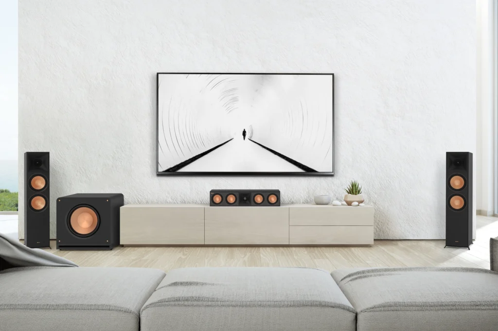 Two black floorstanding speakers, a centre speaker and a subwoofer with copper drivers around a television on a white wall