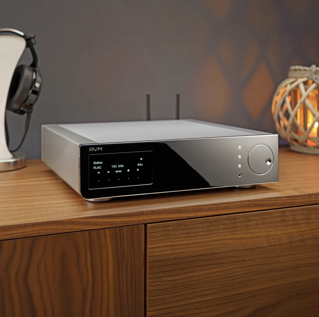A silver AVM streaming amplifier on a walnut sideboard, its display showing a Qobuz FLAC stream at 192 kHz, with headphones alongside.