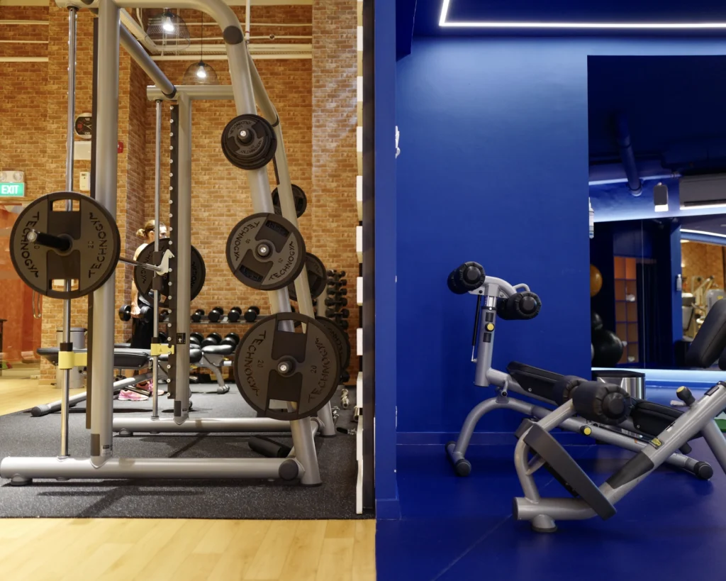 Weight rack against a brick wall in the condominium gym, with a blue-walled training area beyond