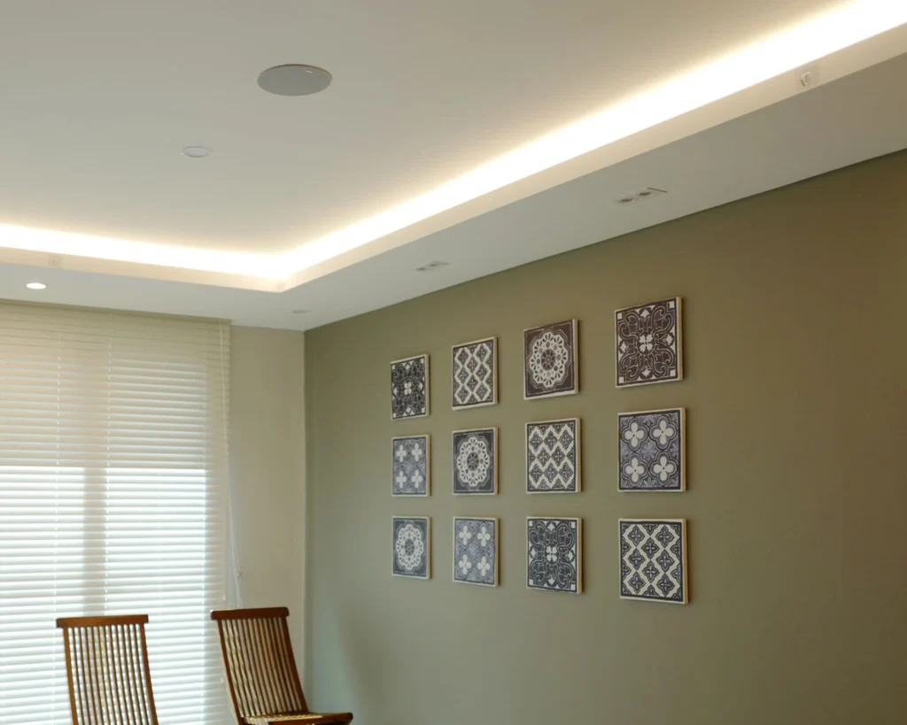 Recessed ceiling speaker and cove lighting above a green feature wall hung with framed tiles