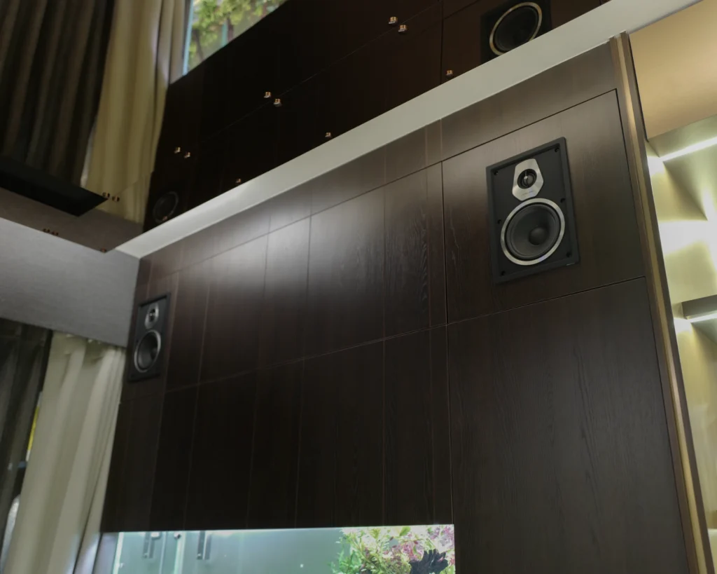 An in-wall speaker set flush into the room's dark wood panelling, with a second on the far column.
