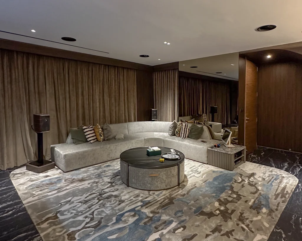 Curved sofa and round coffee table facing a bookshelf speaker on a stand, with ceiling speakers overhead