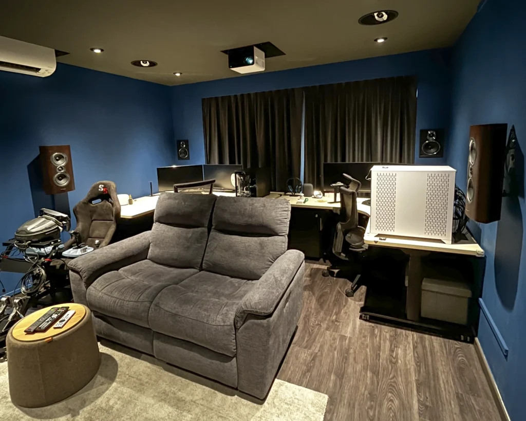 Blue-walled room with a reclining sofa and desk area, with Sonus Faber speakers mounted on the walls