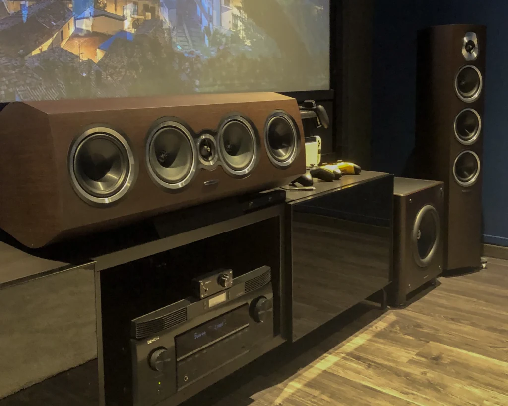 Close-up of a Sonus Faber Sonetto centre speaker above an AV receiver, with a floorstanding speaker and subwoofer beside it