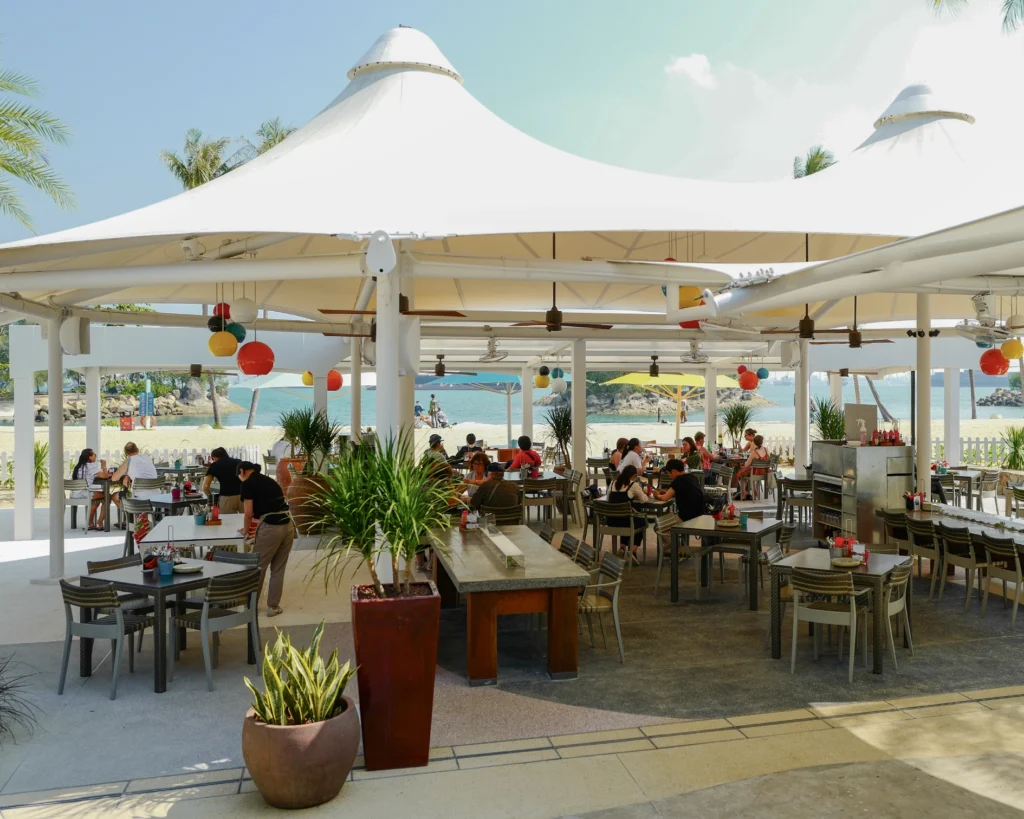 Tables under a white canopy at the beachfront restaurant, with the sea beyond