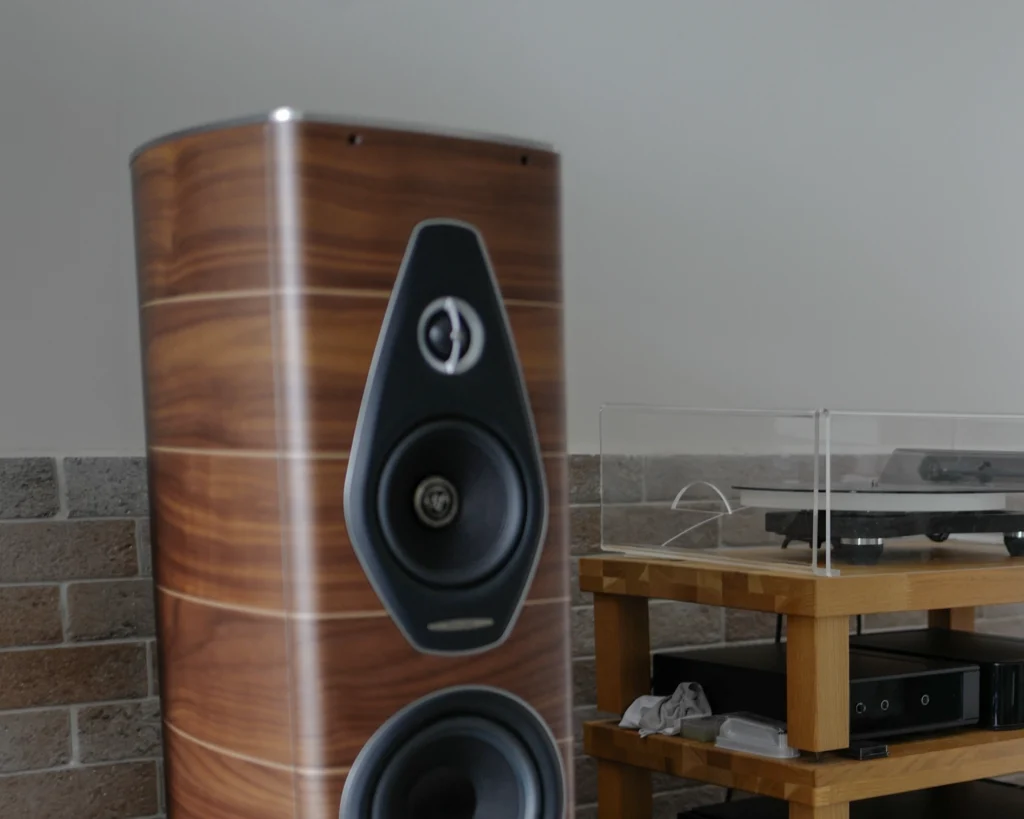Close-up of a walnut Sonus Faber Olympica Nova III speaker, with the turntable rack behind it