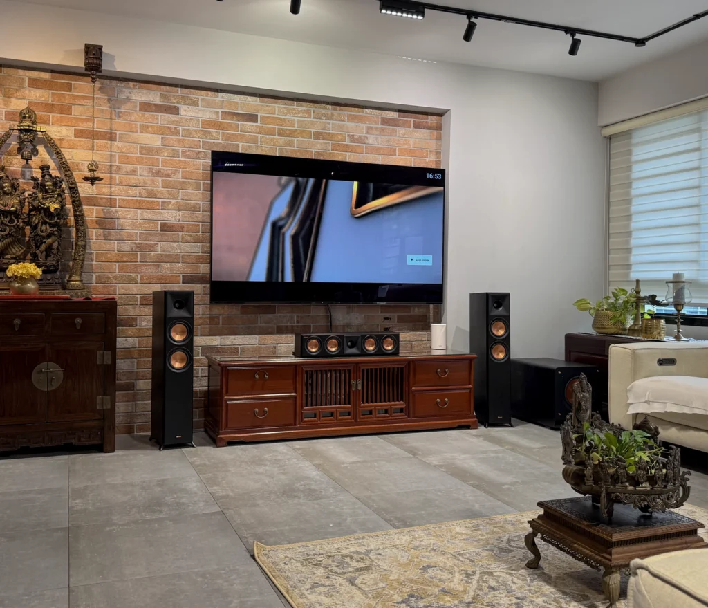 A Klipsch 5.1 system in black: two floorstanders either side of a wooden cabinet, with a wall-mounted TV on exposed brick.