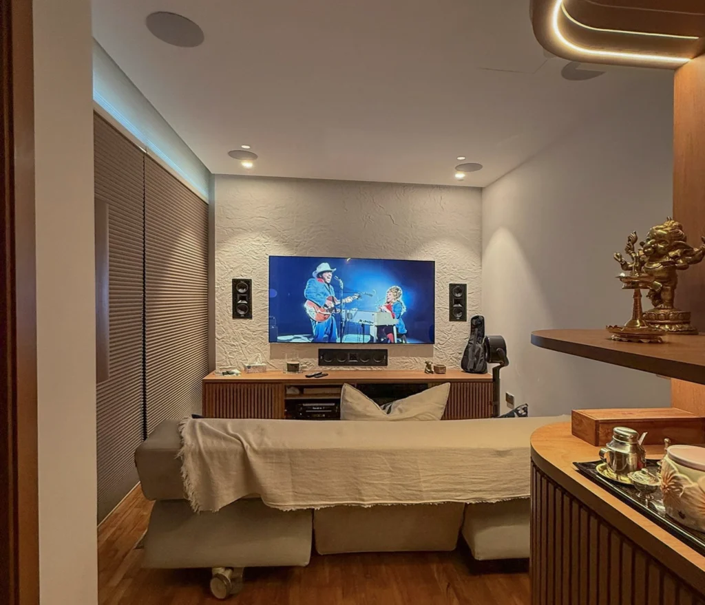 Condo living room seen from behind the sofa, with a wall-mounted TV, flush speakers, a timber console and curved joinery.