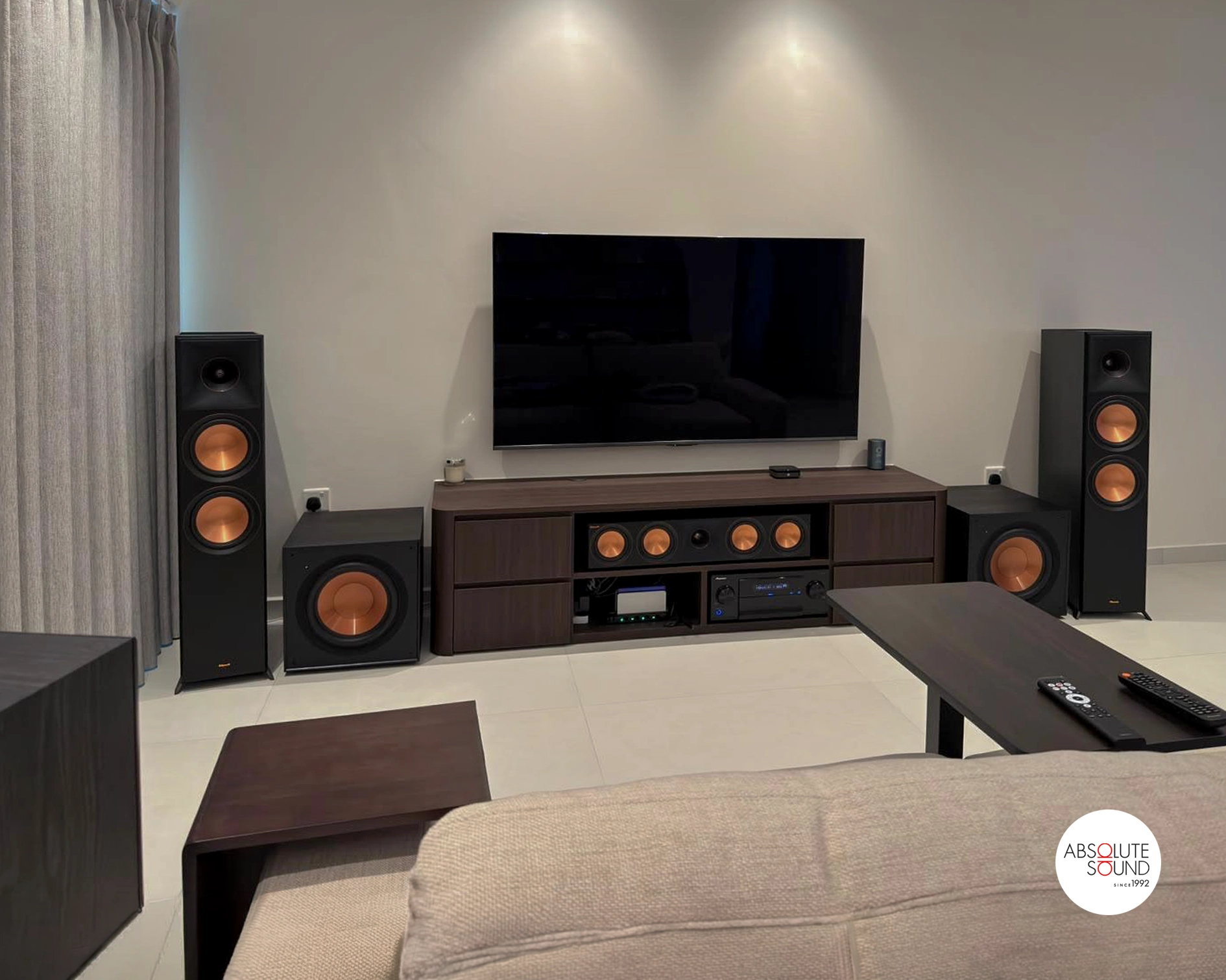 Front wall of a Klipsch 5.2.4 home theatre: two floorstanders, a centre speaker below the TV and a subwoofer at each end of the console