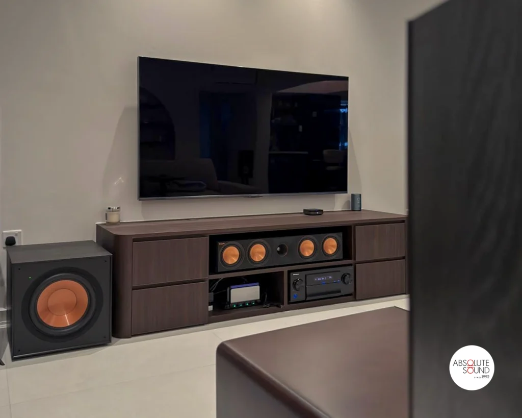 Close view of the media console with the Klipsch centre speaker in the middle shelf, a subwoofer at left and a floorstander at right.