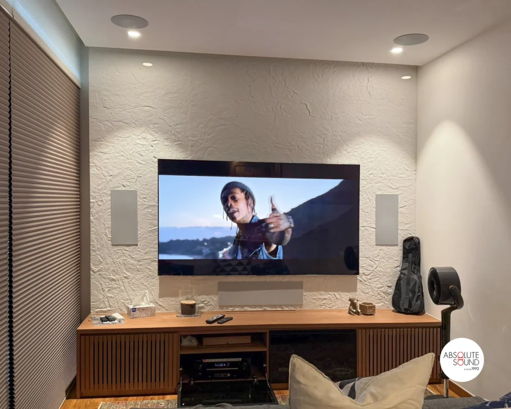 Straight-on view, grilles fitted: white flush panels either side of the TV, a centre strip below, round ceiling grilles.