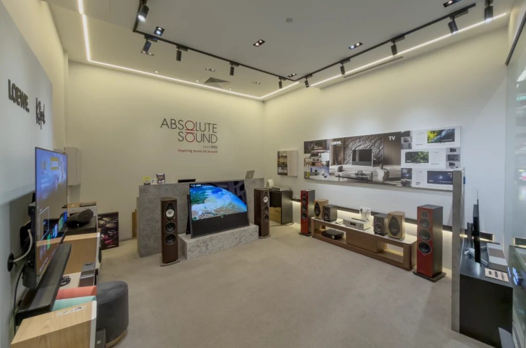 Showroom with the Absolute Sound sign, floorstanding and bookshelf speakers on display, and televisions along the walls